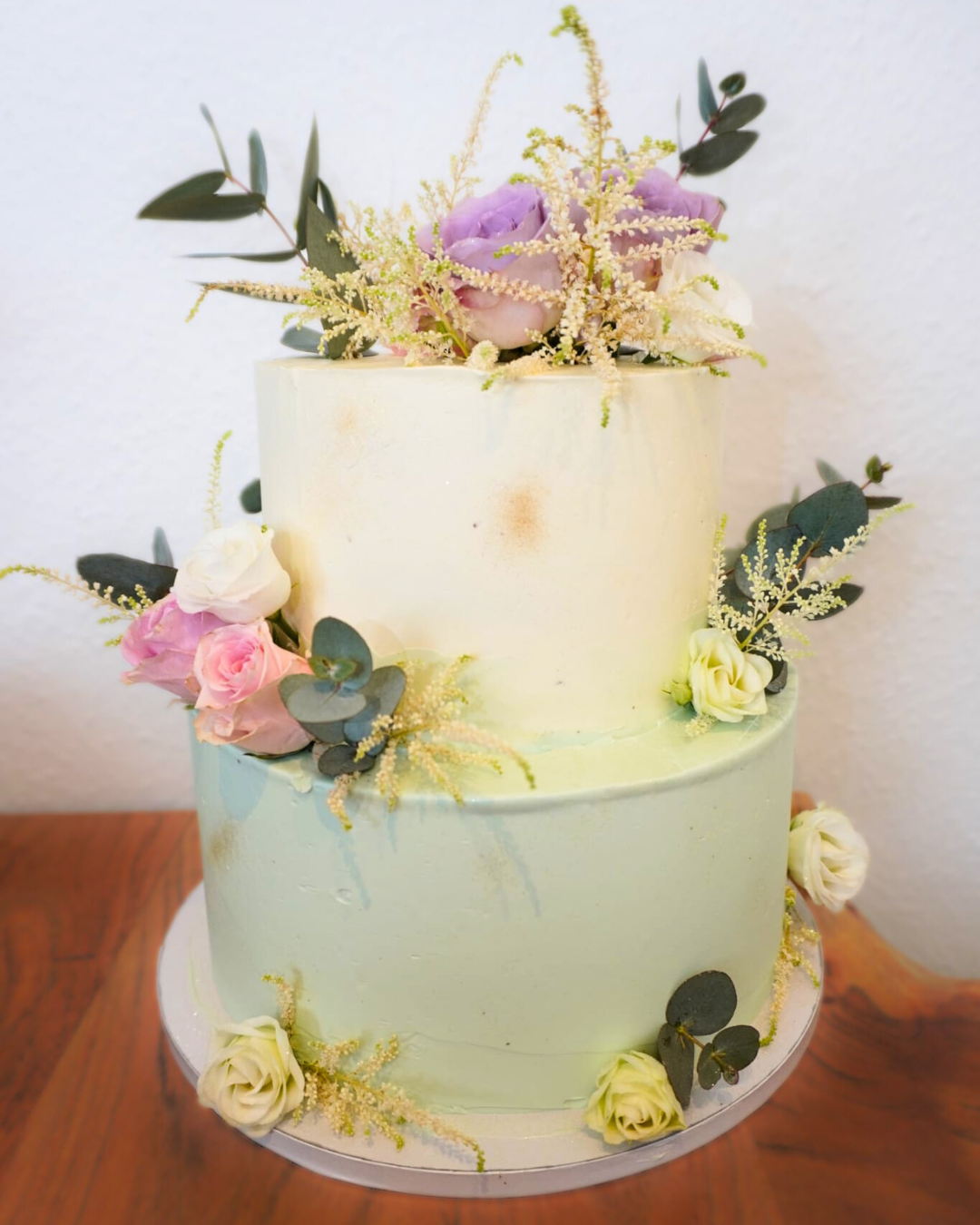 zwei-lagige Torte in sanften Pastellfarben, verziert mit einer Auswahl an Blumen oben drauf