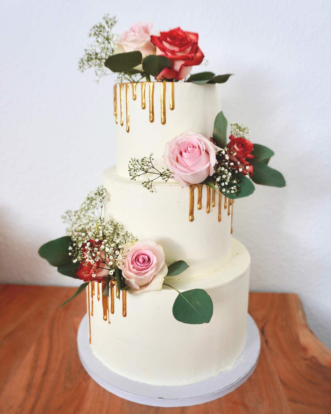 Dreistufige Torte mit zarten Rosen und goldenen Tropfen, perfekt für Hochzeiten oder Jubiläen