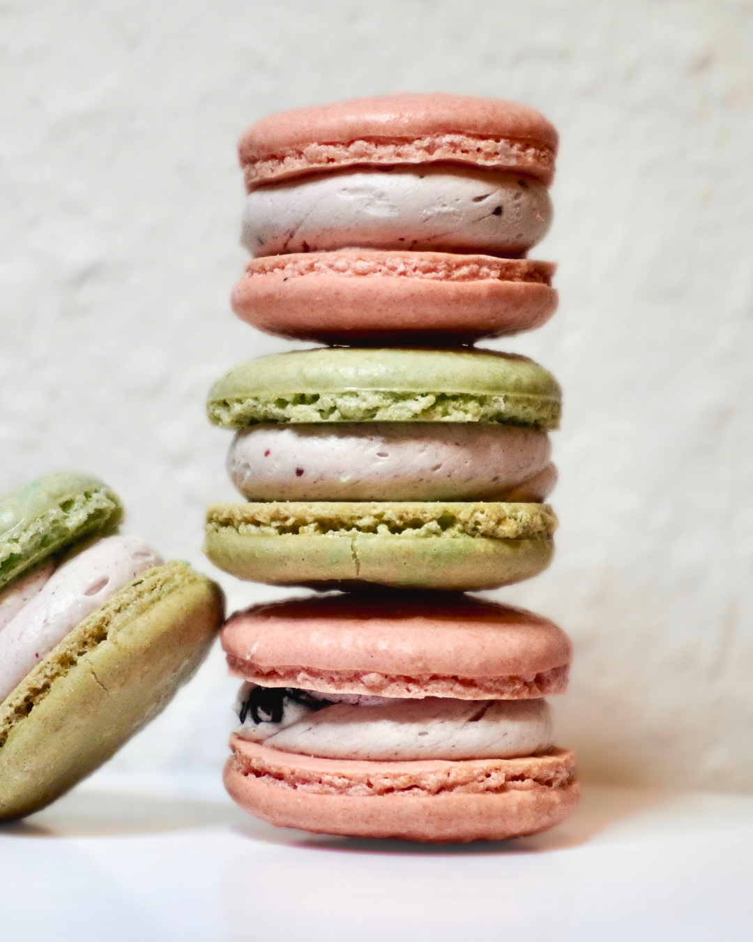Bunte Macarons in verschiedenen Farben, übereinander gestapelt, auf einer weißen Fläche präsentiert
