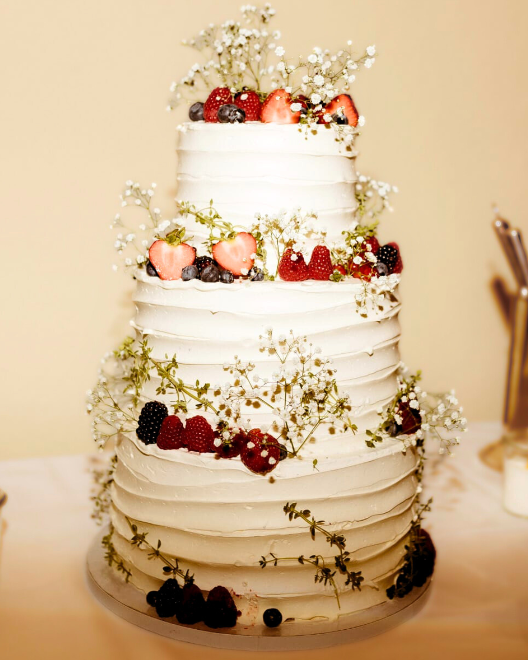 Eine kunstvoll dekorierte Hochzeitstorte, belegt mit saftigen Beeren und zarten Blumen, strahlt festliche Eleganz aus